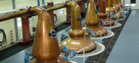 Image of several copper pot stills in a warehouse setting.