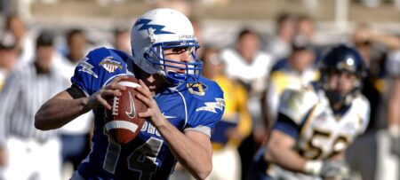 Image of a foorball quarterback holding the ball and wearing a blue jersey and white helmet with a lightening bolt.