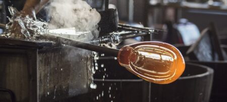 Molten glass being shaped into a sphere with smoke in the background.