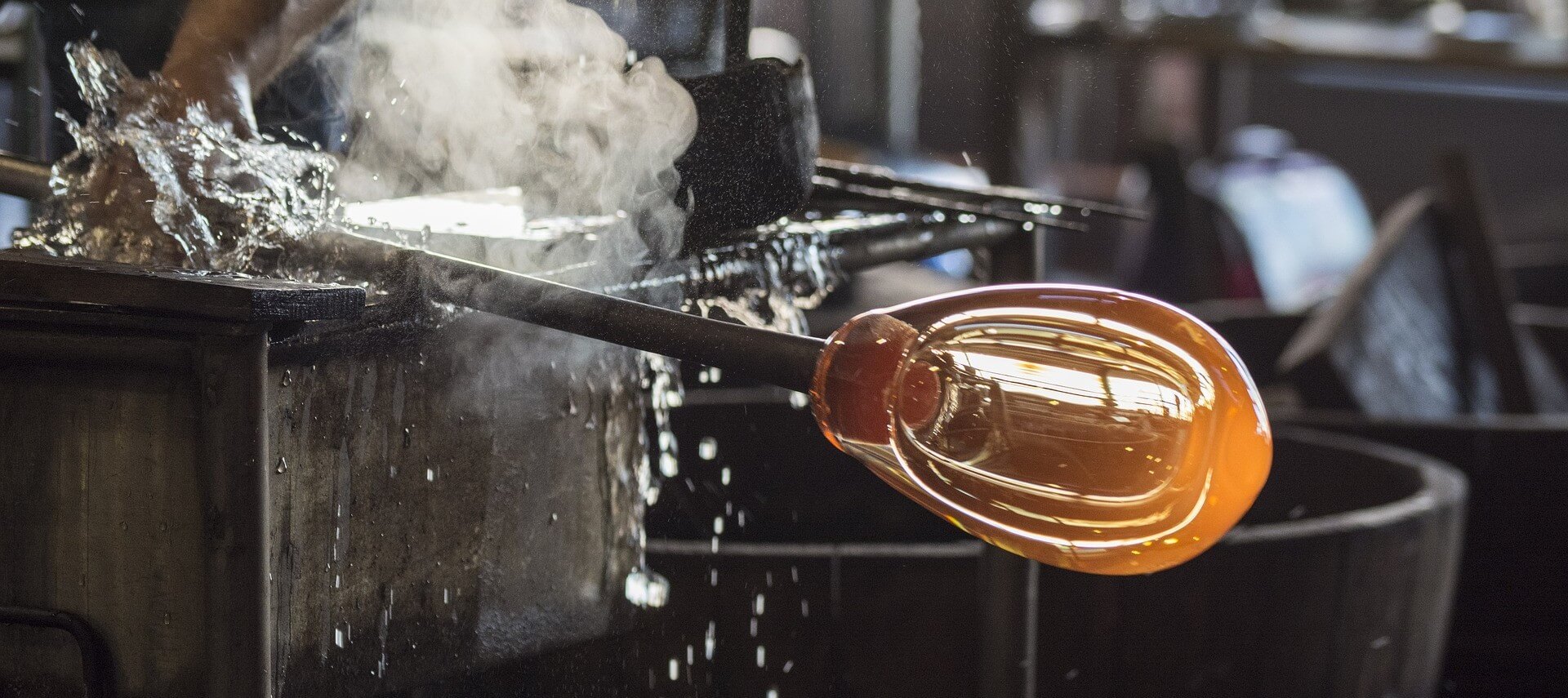 Molten glass being shaped into a sphere with smoke in the background.