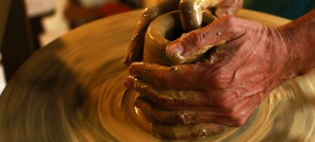 Artists hands molding wet clay on a potters wheel.