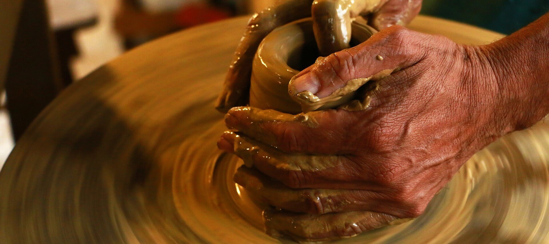 Artists hands molding wet clay on a potters wheel.