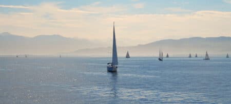 A picture of sailboats on a lake with blue water and hills in the background.