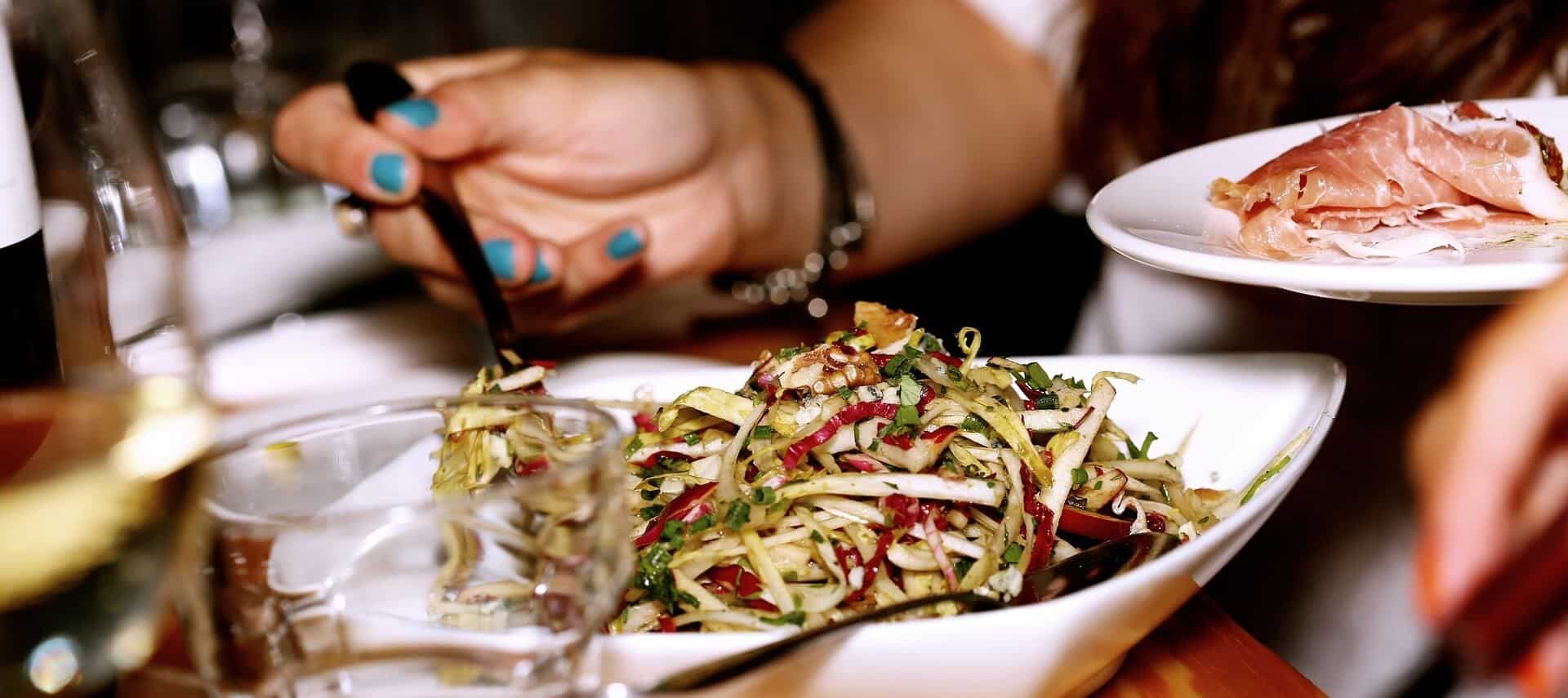 A person with turquoise fingernails is serving a salad with a fork.
